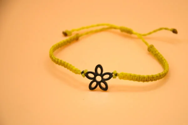Micro macrame náramek s nerezovým přívěskem ve tvaru květin doplněný posuvným uzlíkem na přizpůsobení velikosti.
